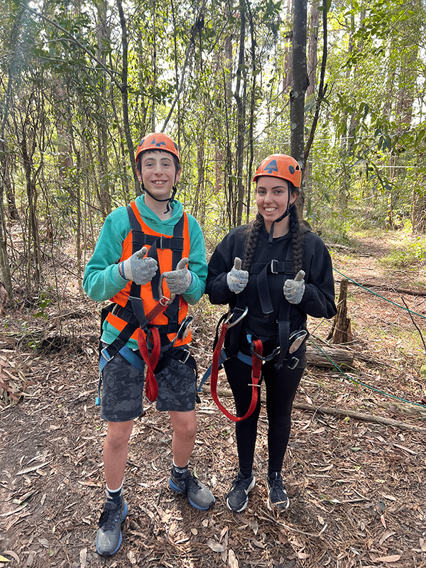 Two people wearing safety harnesses and helmets, smiling in the bush